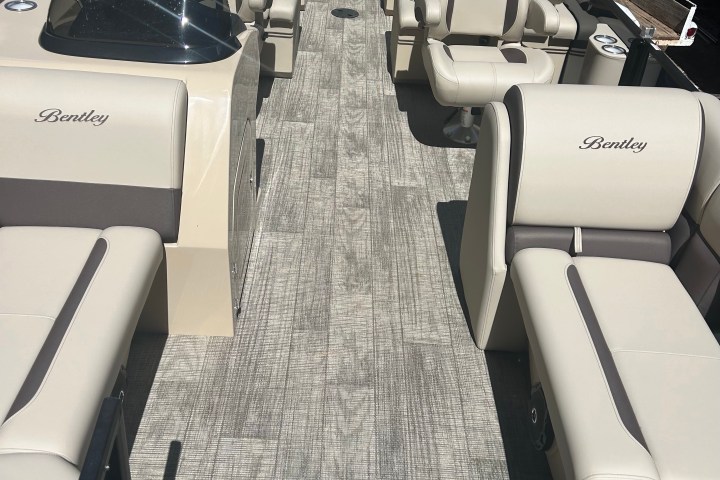 Interior of a pontoon boat with beige seats and grey flooring, branded 'Bentley'.