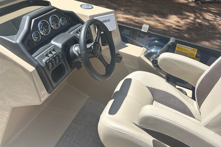 Boat cockpit with steering wheel, control panel, and beige seat.