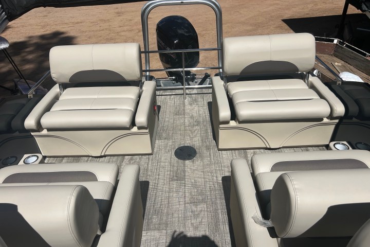 Interior of a pontoon boat with beige seating and a motor at the back.